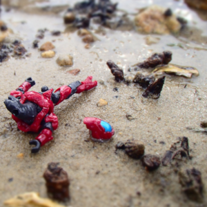 Armored alien with missing leg and helmet aside on damp sand with wood debris