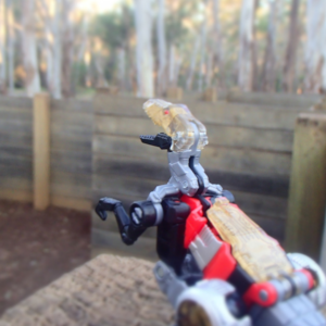 A robotic velociraptor perches on a wooden wall looking out into a giant wooden maze.