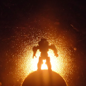 Silhouette of an armored space soldier standing atop a sphere with radiant yellow light glowing behind it them.