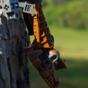 Close shot of a brown Bionicle's legs dangling off a wooden fenceposts with its arms at its side.