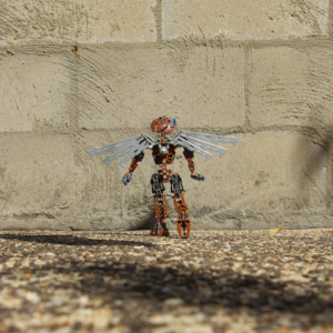 Wide shot of a brown Bionicle with robotic wings steps towards a brick wall while looking far upwards.